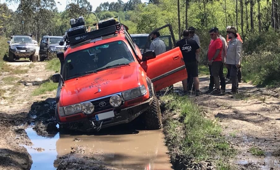 Todoterreno rojo hundido en un barrizal encharcado, con varias personas alrededor preparando la recuperación.