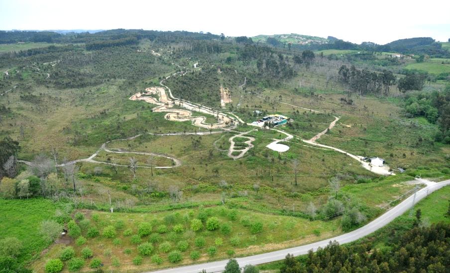 Vista aérea de la finca: prados, pistas de tierra serpenteando entre el arbolado y la carretera de acceso al fondo.