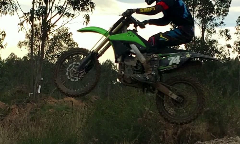 Piloto de motocross en pleno salto sobre la zona de saltos del parque, al atardecer.