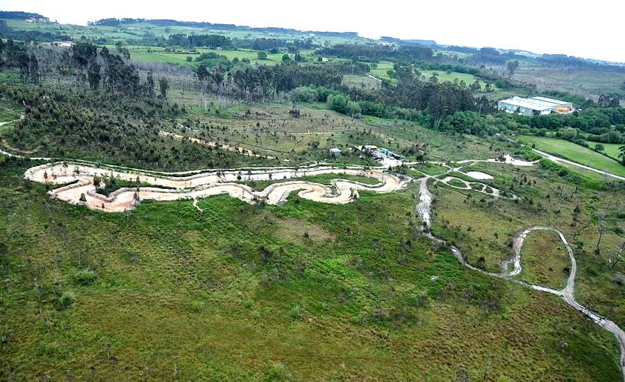 Vista aérea del trazado de pistas del parque, dibujado en claro sobre el prado, con el valle y el caserío al fondo.